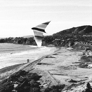 Black and white photo of a hang-glider in the sky over the beach