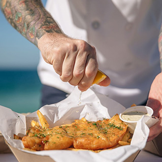 Person squeezing lemon over battered fish